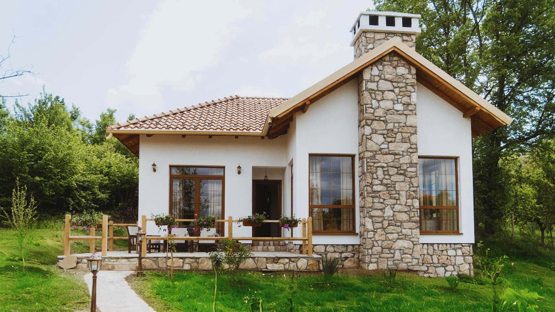 Bela kamena kuća sa dimnjakom okružena zelenilom